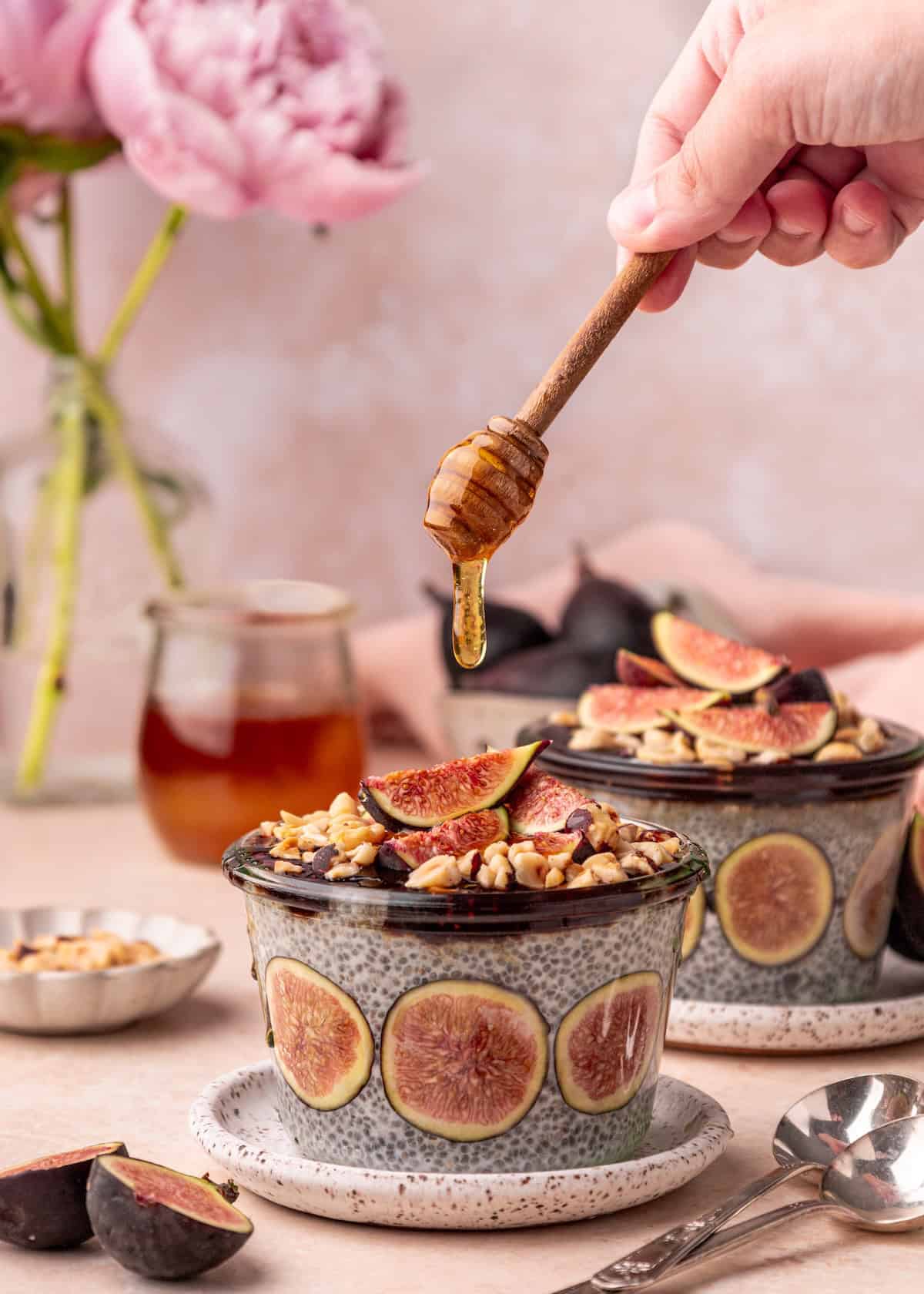 A hand drizzles honey over Fig Chia Pudding bowls topped with figs and nuts.