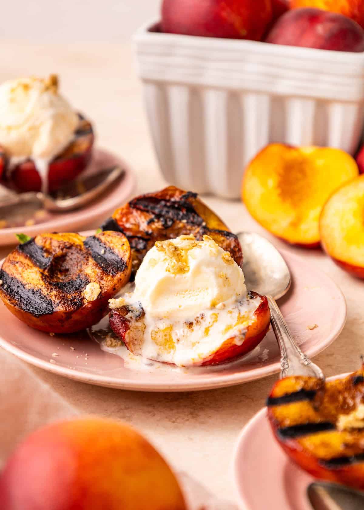 Honey Grilled Peaches topped with vanilla ice cream and honey on a pink plate.