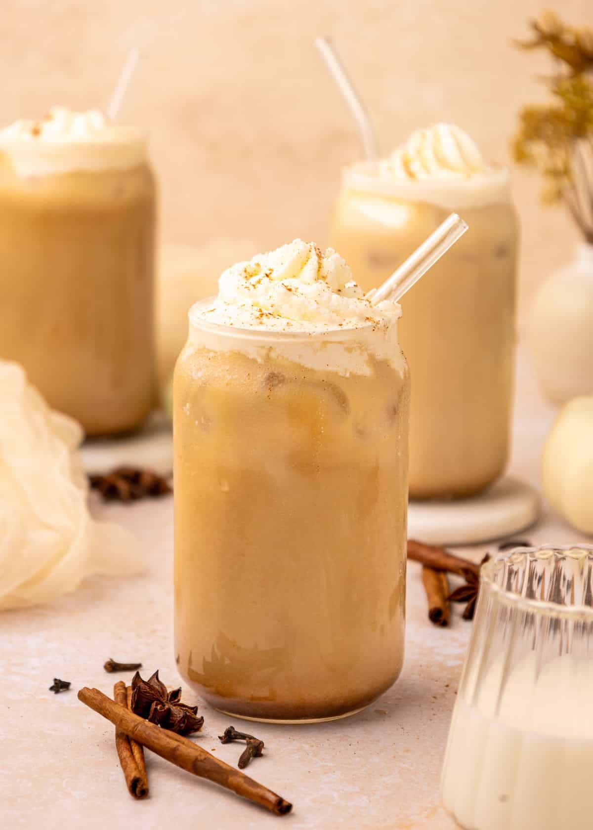 Iced Pumpkin Spice Latte topped with whipped cream, served with a straw and cinnamon sticks.