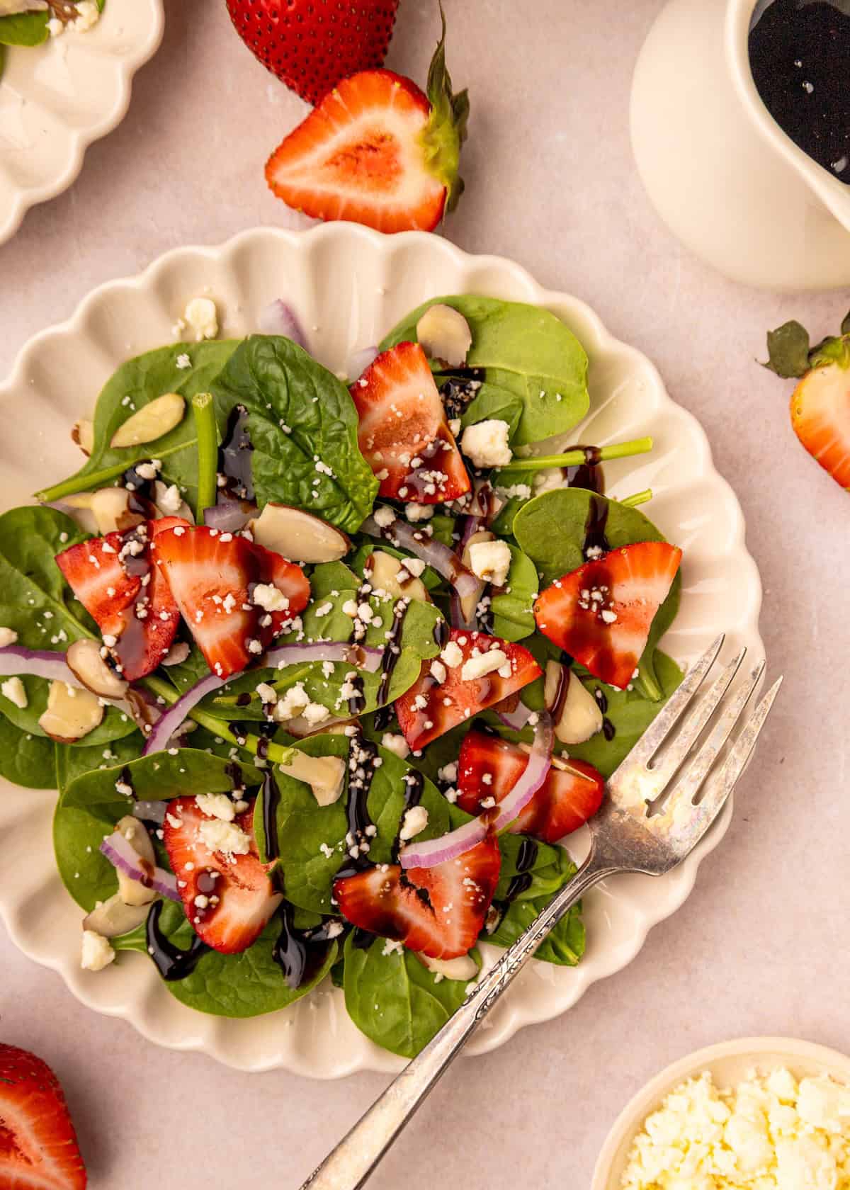 Strawberry spinach salad with feta, almonds, and balsamic dressing served on a white plate.