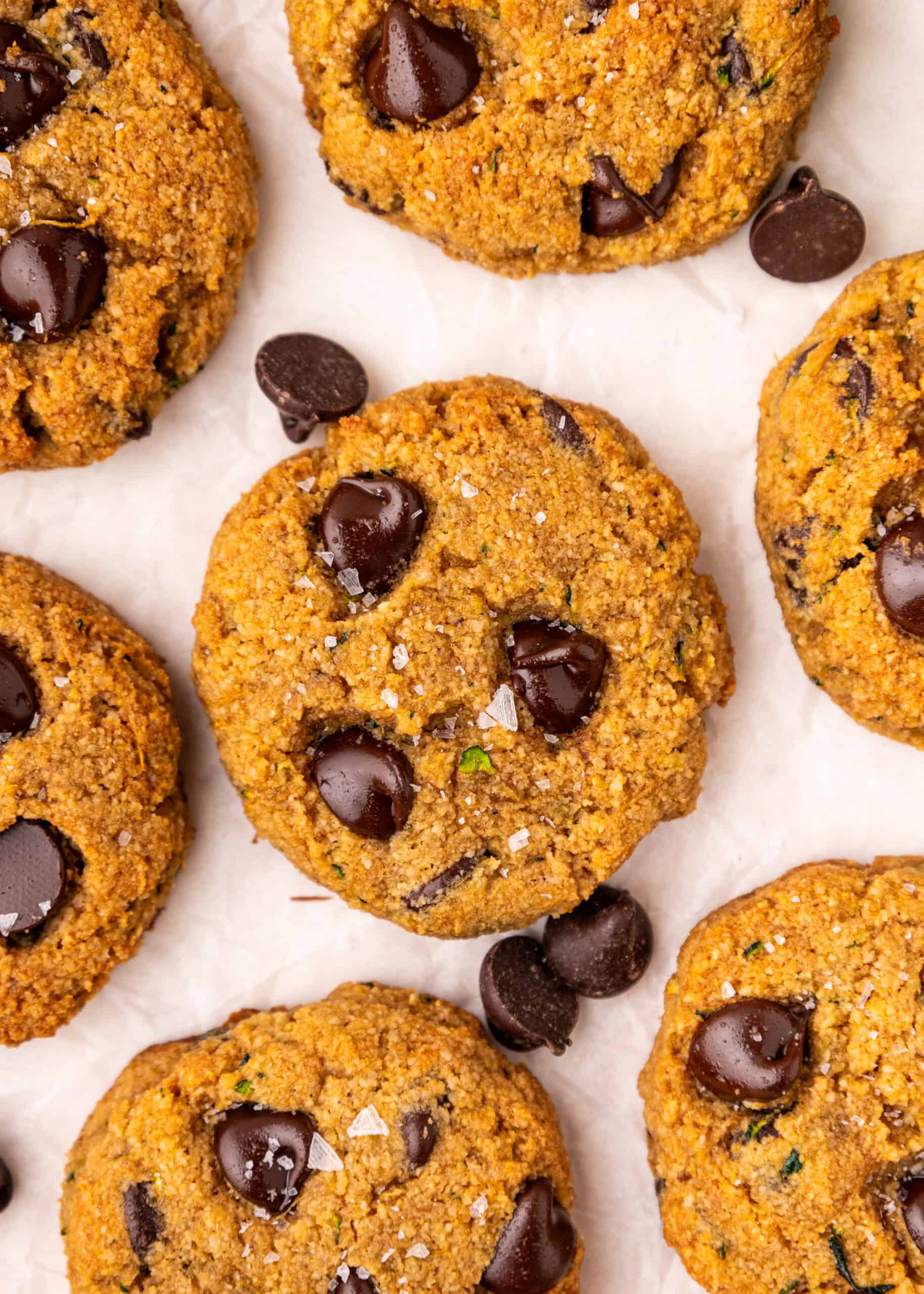 Chocolate Chip Zucchini Cookies topped with sea salt on parchment paper, viewed from above.
