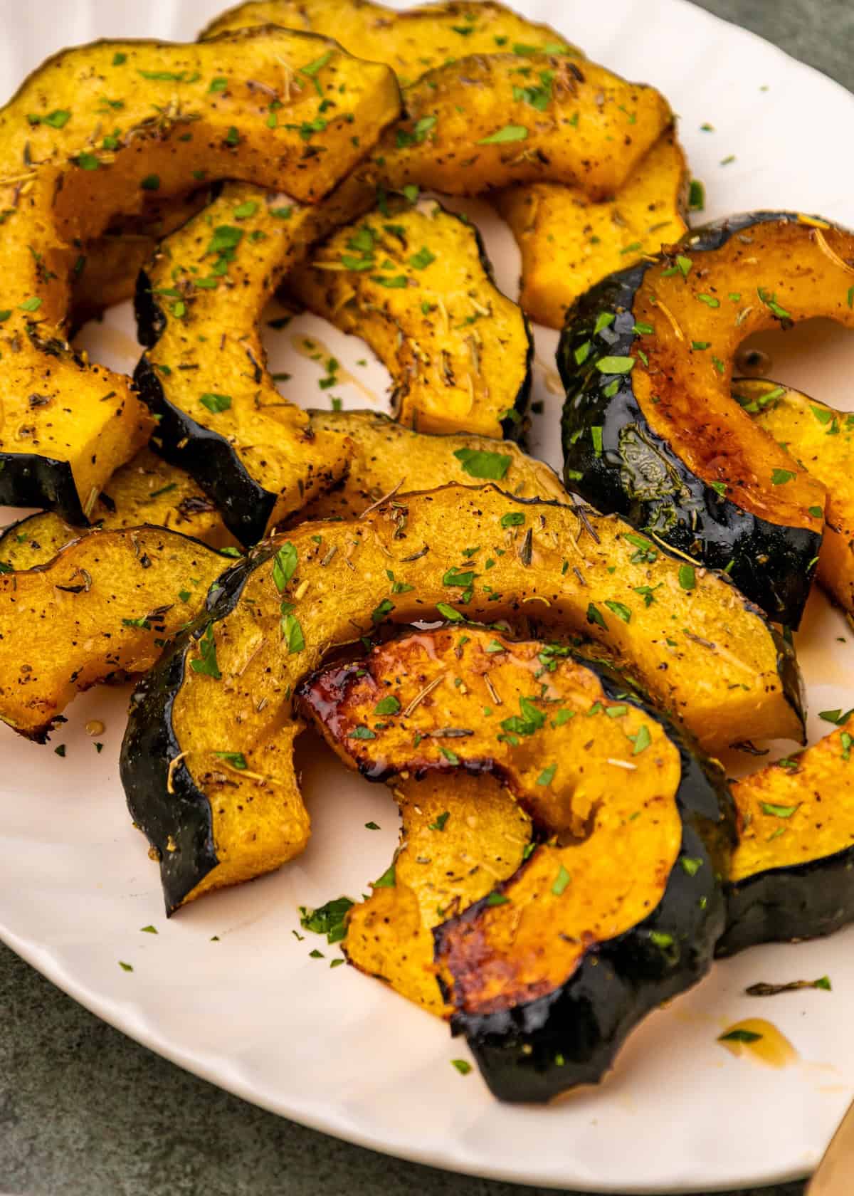 Sliced Roasted Acorn Squash with herbs served on a white plate.