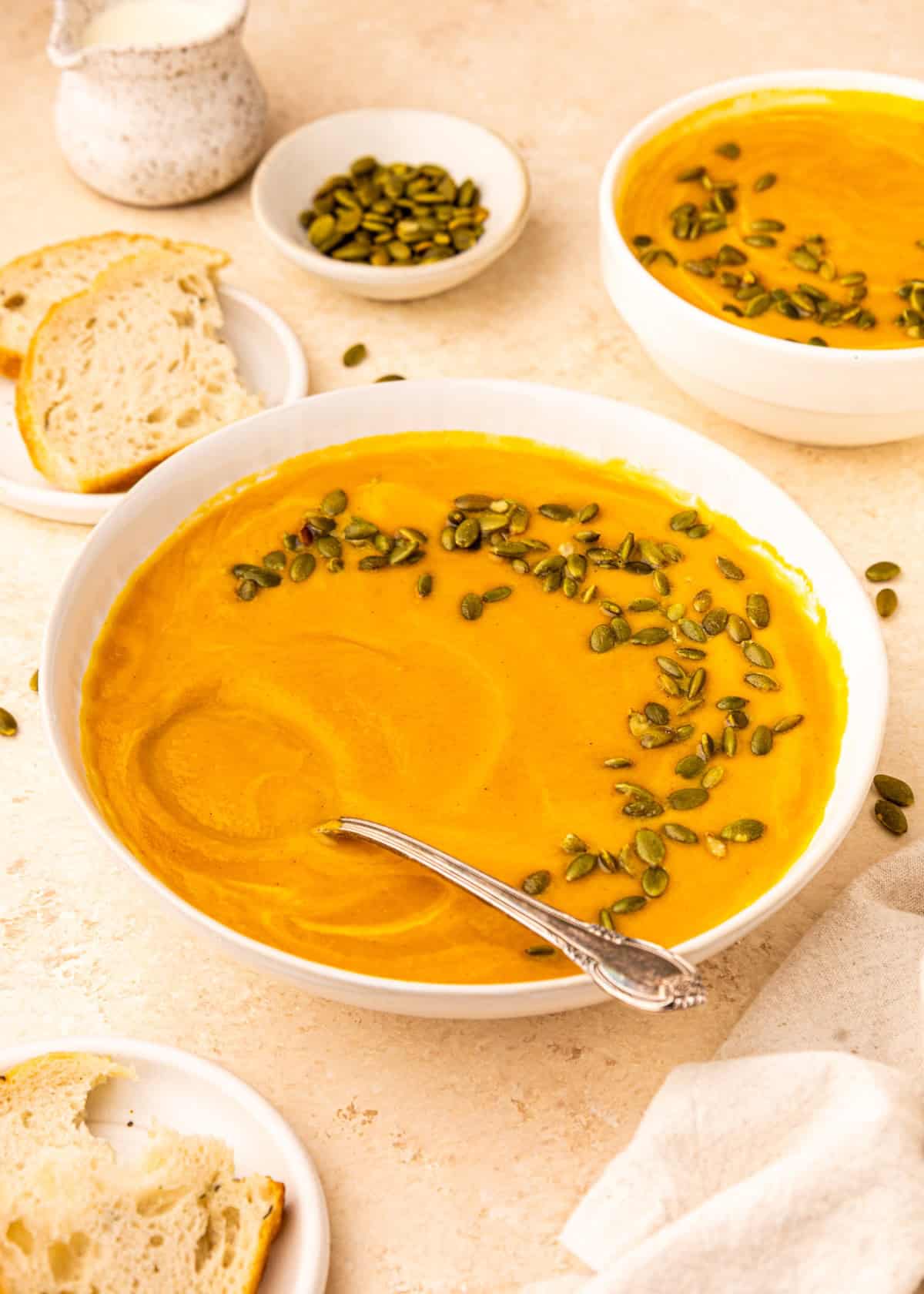 Bowl of Crockpot Sweet Potato Soup topped with pumpkin seeds, served with bread slices.