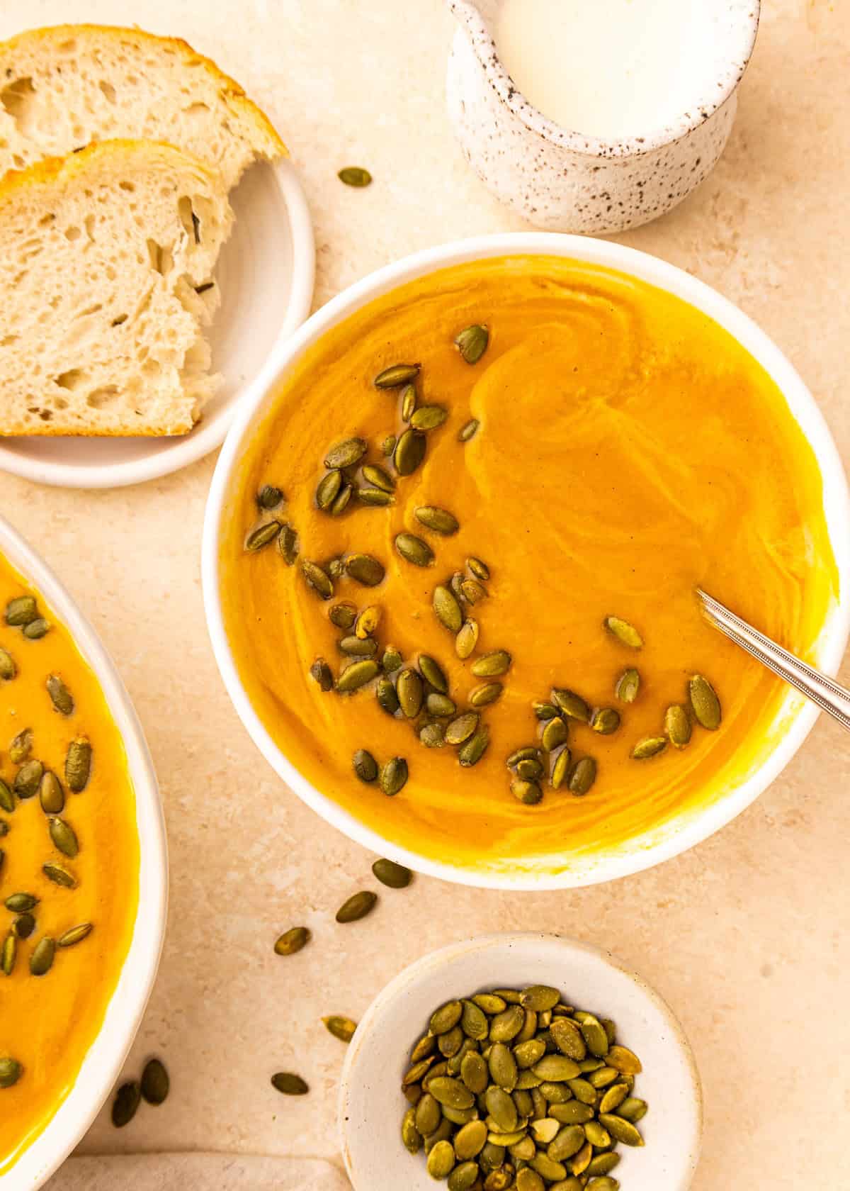 Bowl of Crockpot Sweet Potato Soup topped with pumpkin seeds, with bread and seeds on the side.