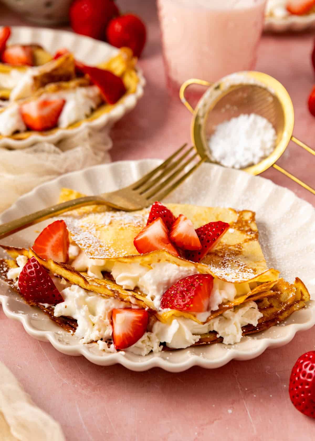 Almond Flour Crepes filled with whipped cream and strawberries, dusted with powdered sugar.
