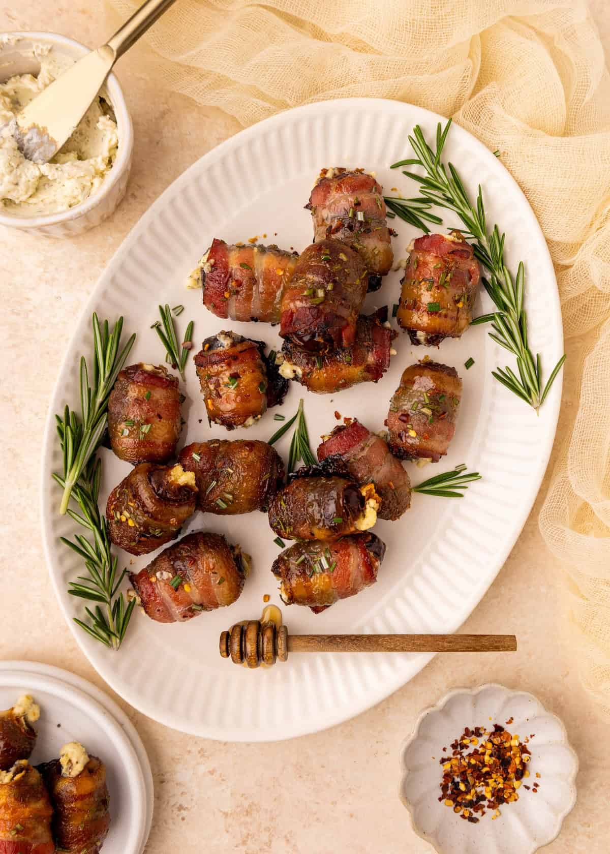 Bacon Wrapped Dates on a white platter, garnished with rosemary sprigs.