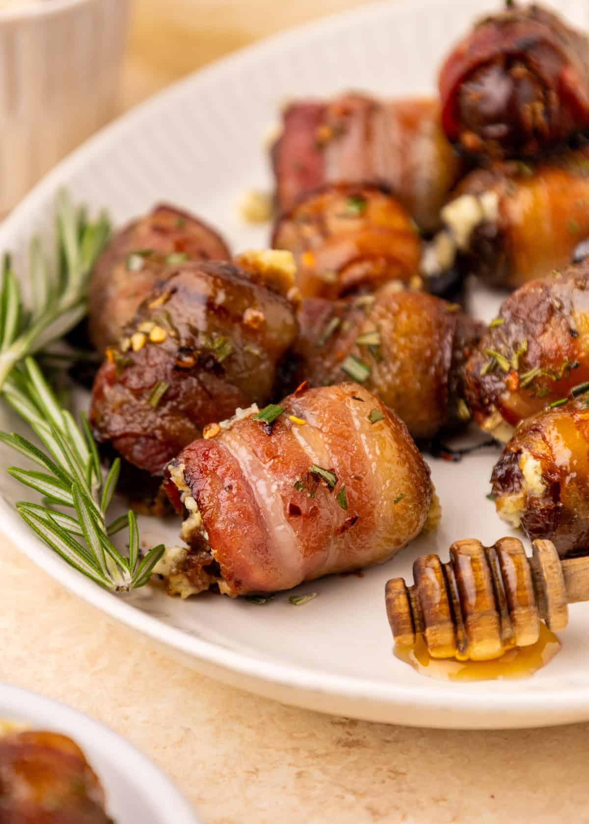 Bacon Wrapped Dates with cheese, garnished with rosemary and served with a honey dipper.