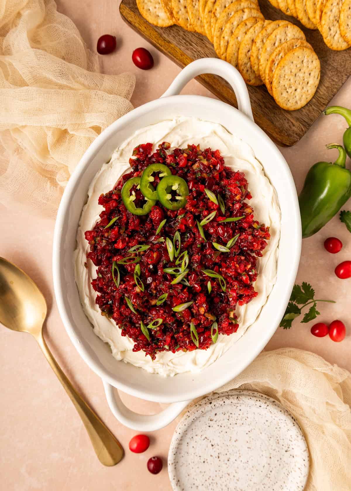 Oval dish with Cranberry Jalapeno Dip, topped with salsa and jalapeños, crackers beside it.