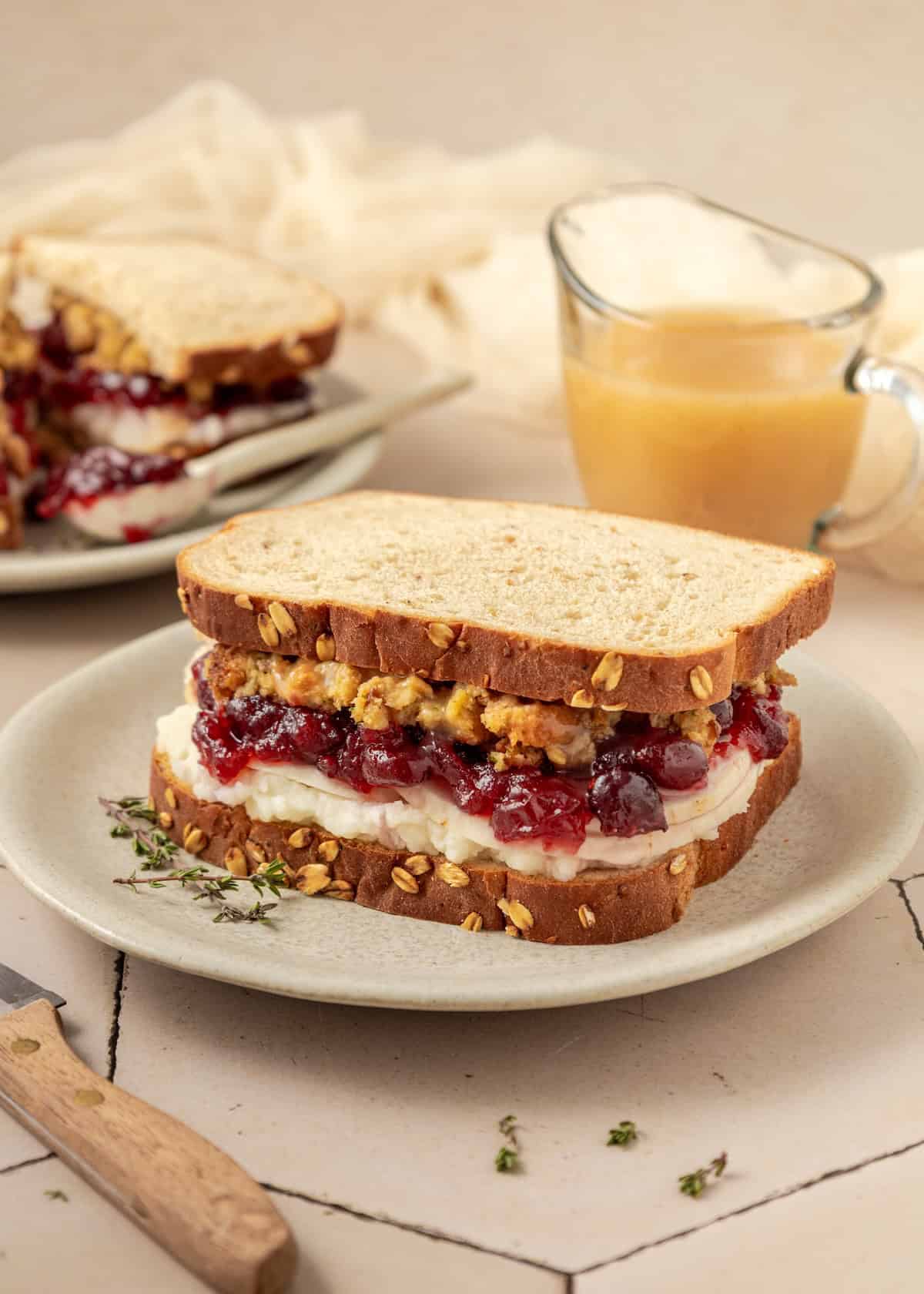 Thanksgiving Sandwich with turkey, cranberry sauce, and stuffing on oat bread, served on a plate.