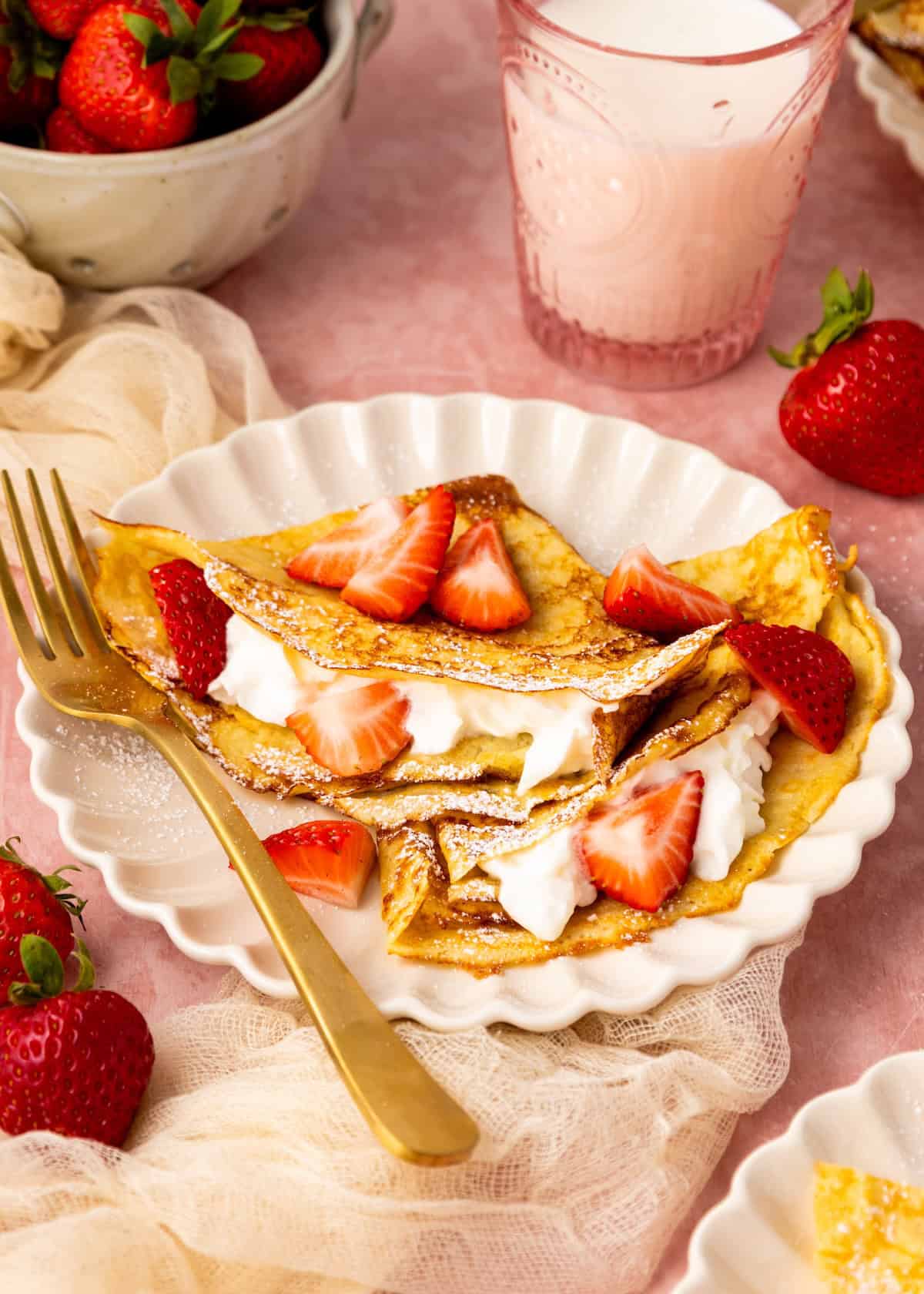 Almond Flour Crepes with whipped cream and strawberries on a white plate, next to milk.
