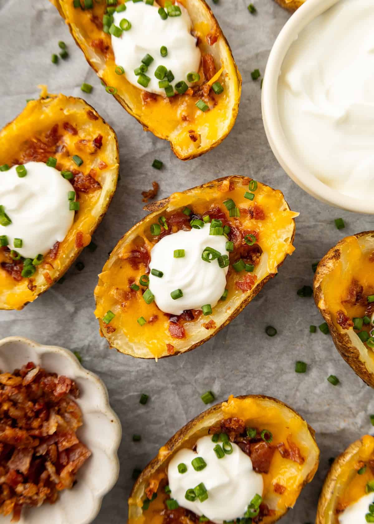 Game Day Recipes: Baked potato skins with cheese, bacon, sour cream, and chives on parchment.