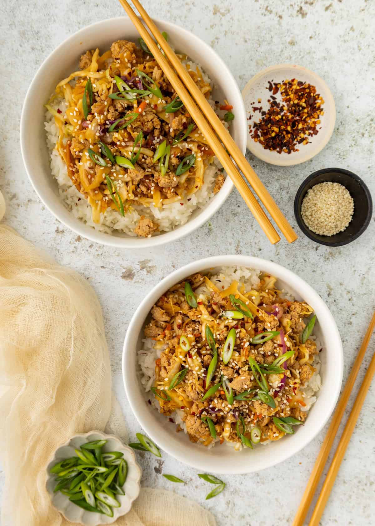 Two Egg Roll Bowls with stir-fried meat, green onions, sesame seeds, and chopsticks.