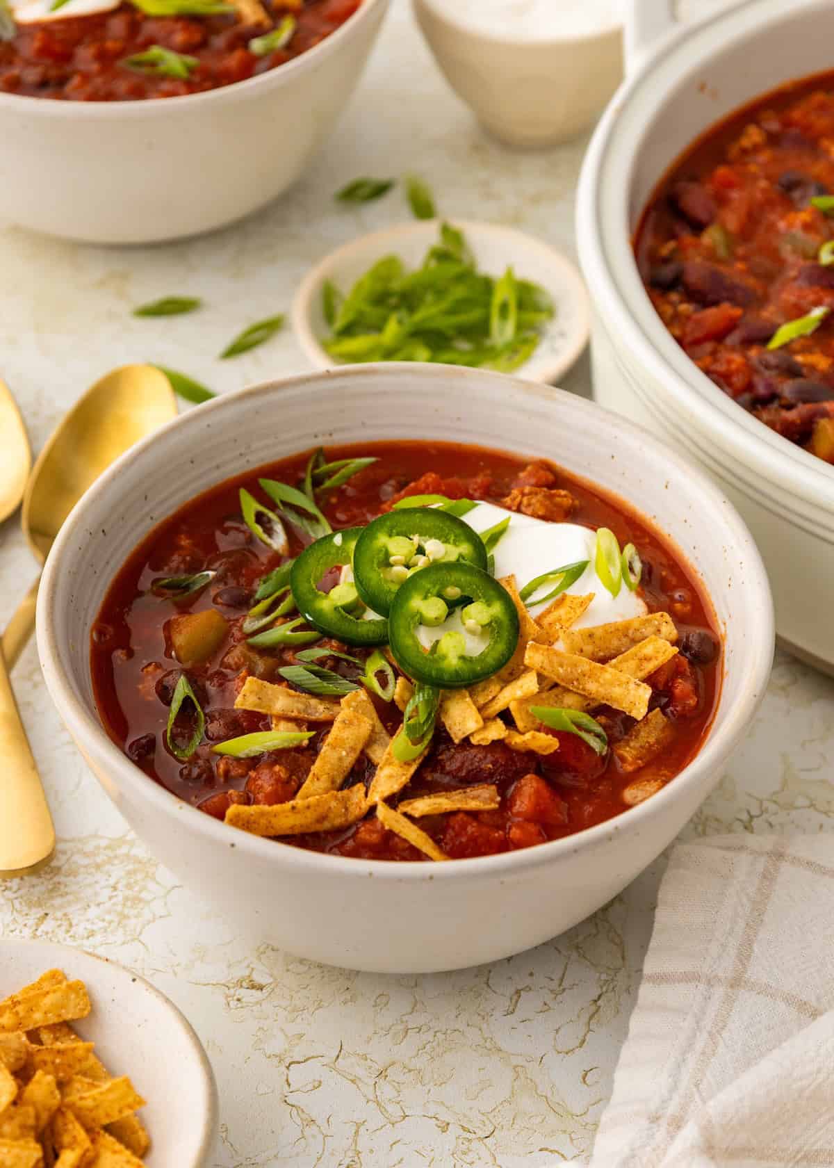 A bowl of ground turkey chili topped with sour cream, sliced jalapeños, and corn chips.