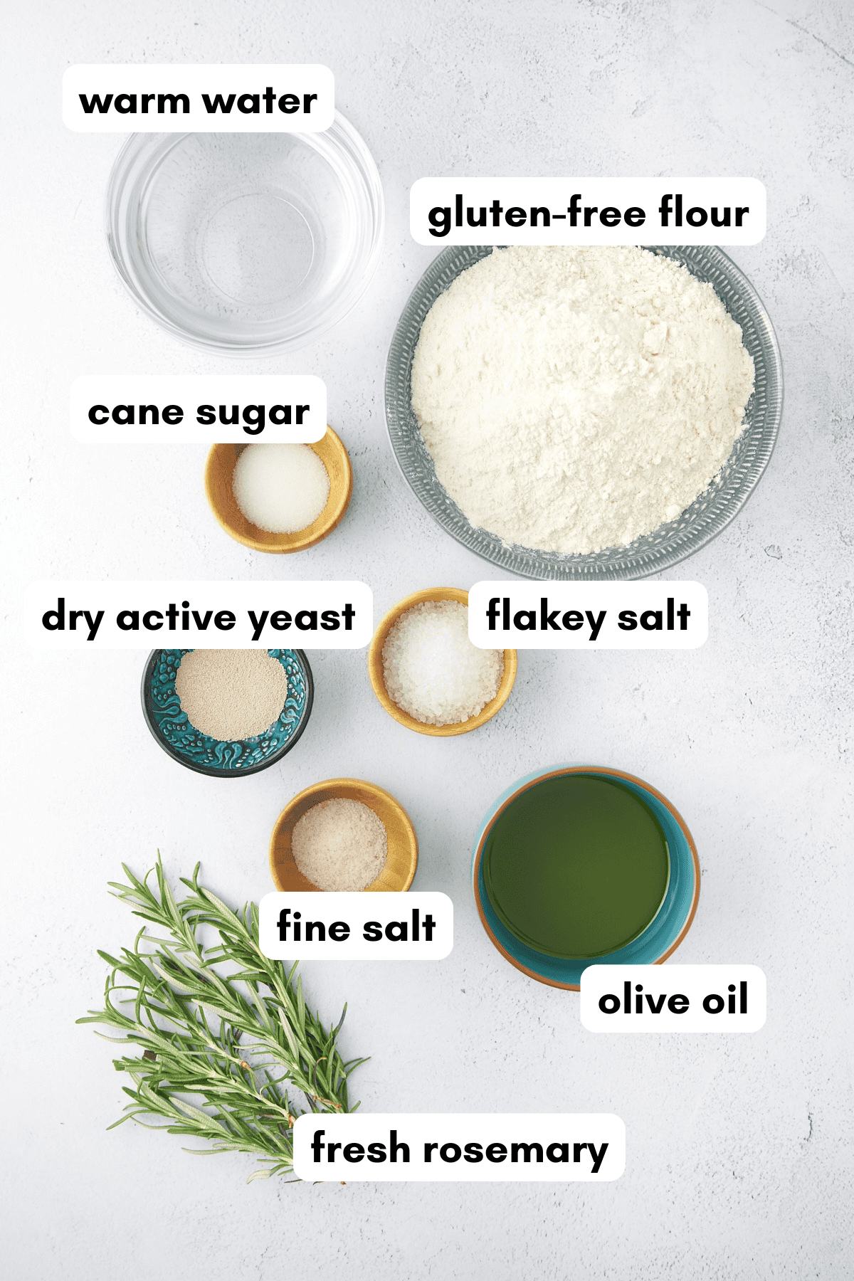 Bowls of gluten-free flour, yeast, salts, cane sugar, olive oil, water, and fresh rosemary.