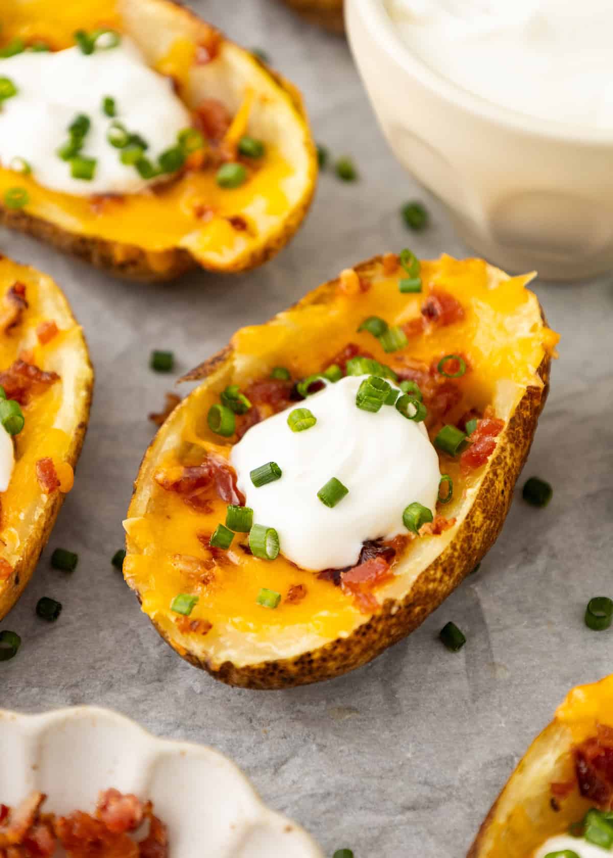 Potato skins with cheese, bacon, sour cream, and chives on a gray surface.