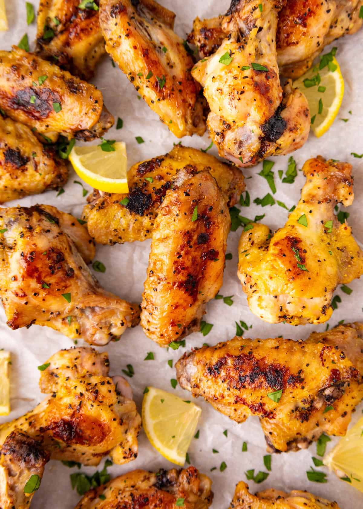 Grilled chicken wings with herbs and lemon wedges on parchment paper.