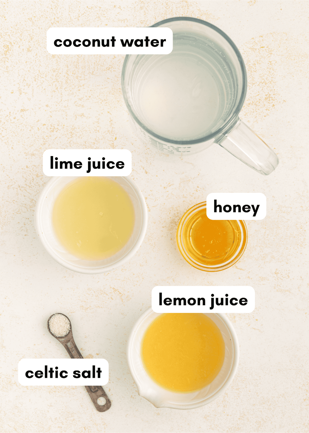 A mug and bowls of coconut water, lime juice, honey, lemon juice, and a spoon of celtic salt.