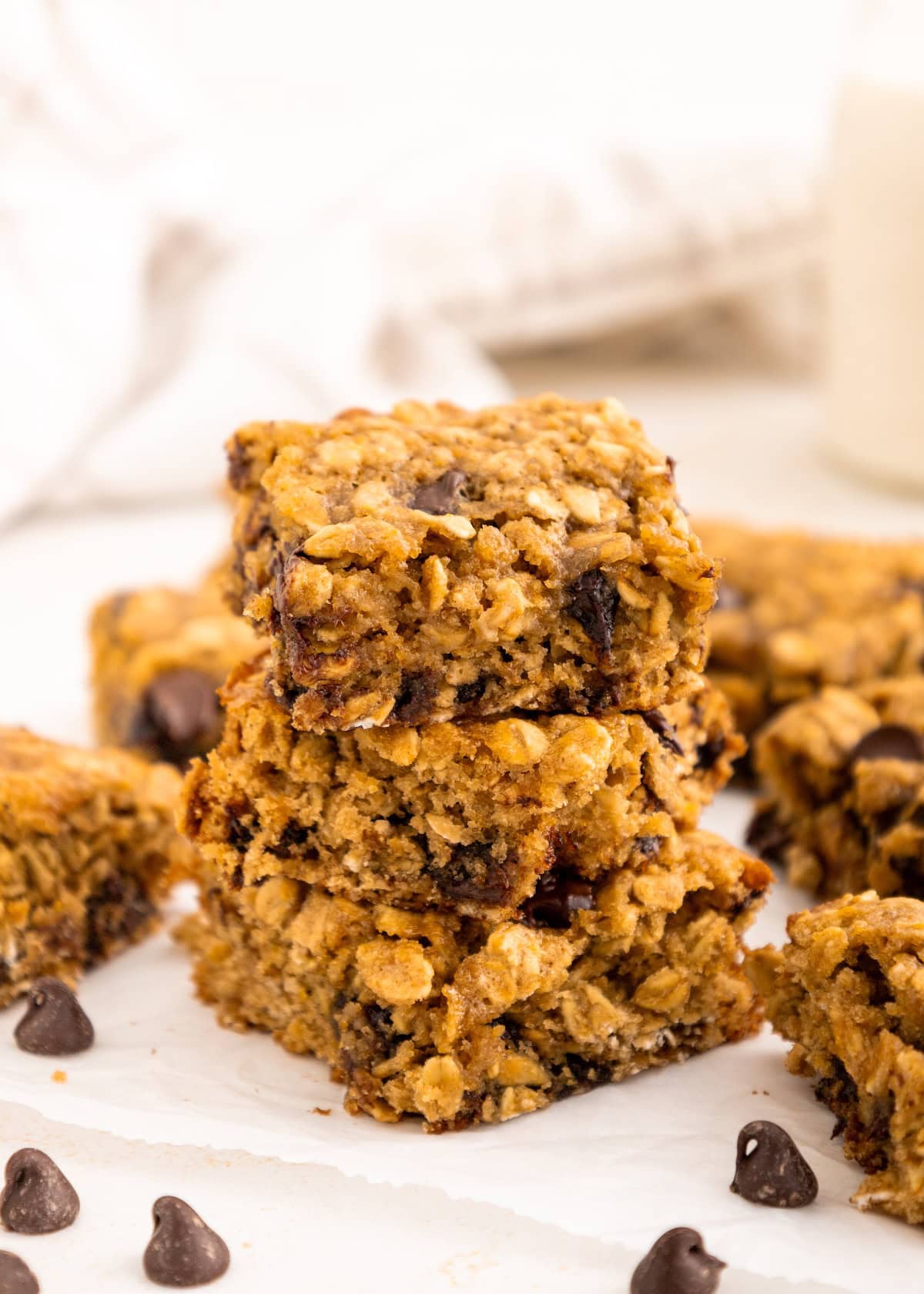 A stack of oatmeal chocolate chip bars on parchment paper with chocolate chips nearby.