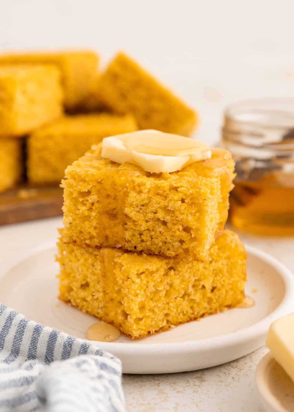 Two pieces of cornbread stacked with butter and honey on top, on a white plate.