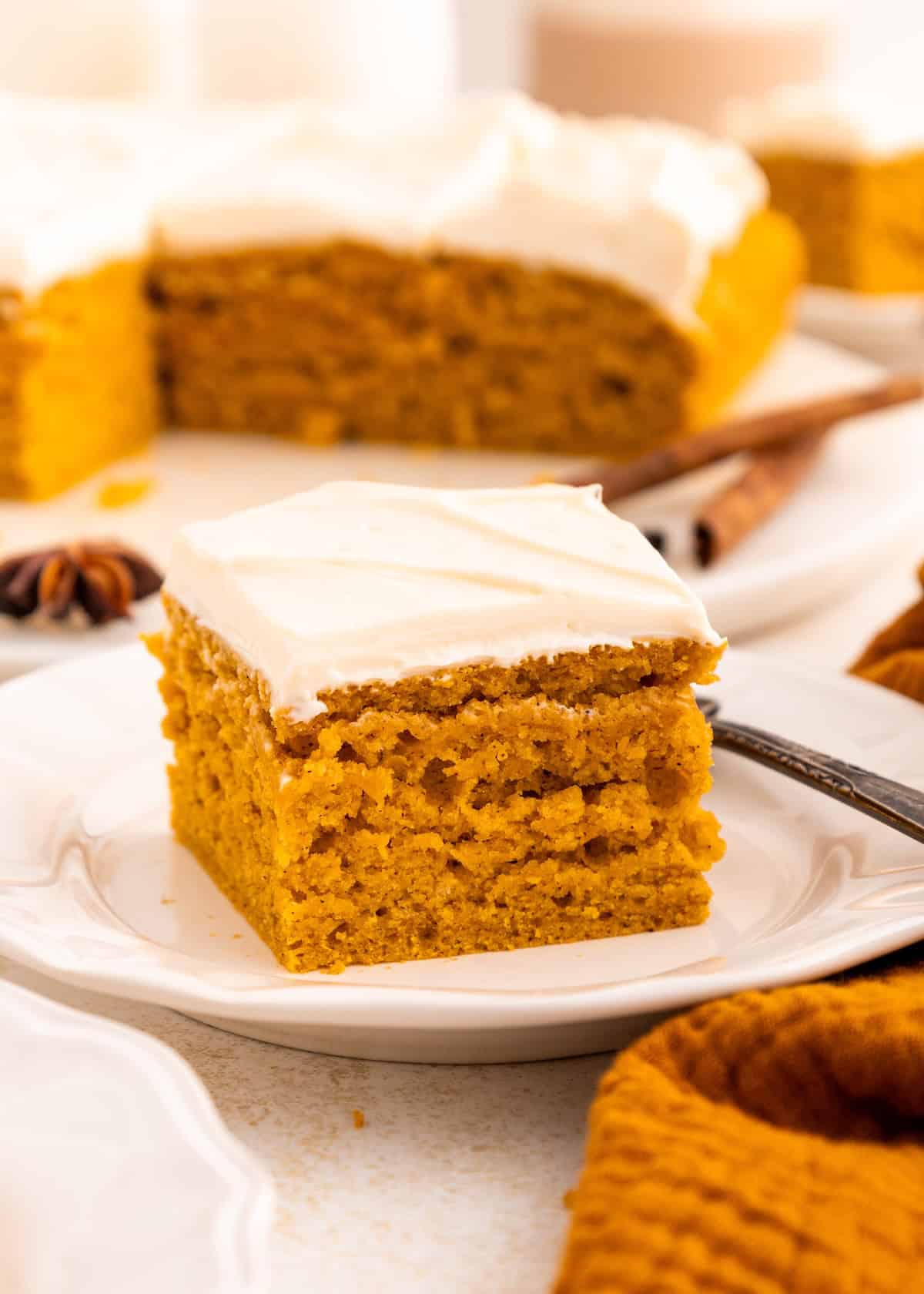 A slice of gluten-free pumpkin cake on a plate, with a whole cake in the background.