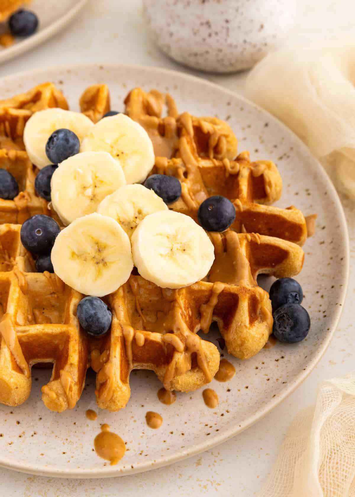 Waffle topped with banana slices, blueberries, and a drizzle of peanut butter on a plate.